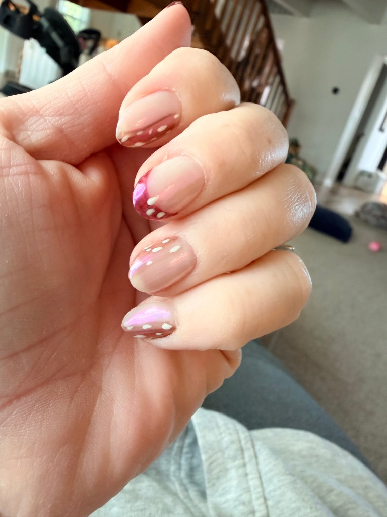 A close-up of a hand displaying manicured nails with a pink ombre design, white speckles, and a glossy finish.