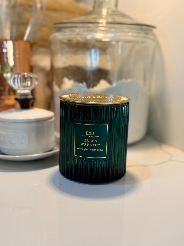 A green glass candle labeled 'Green Wreath' sitting on a countertop, surrounded by decorative kitchen items.